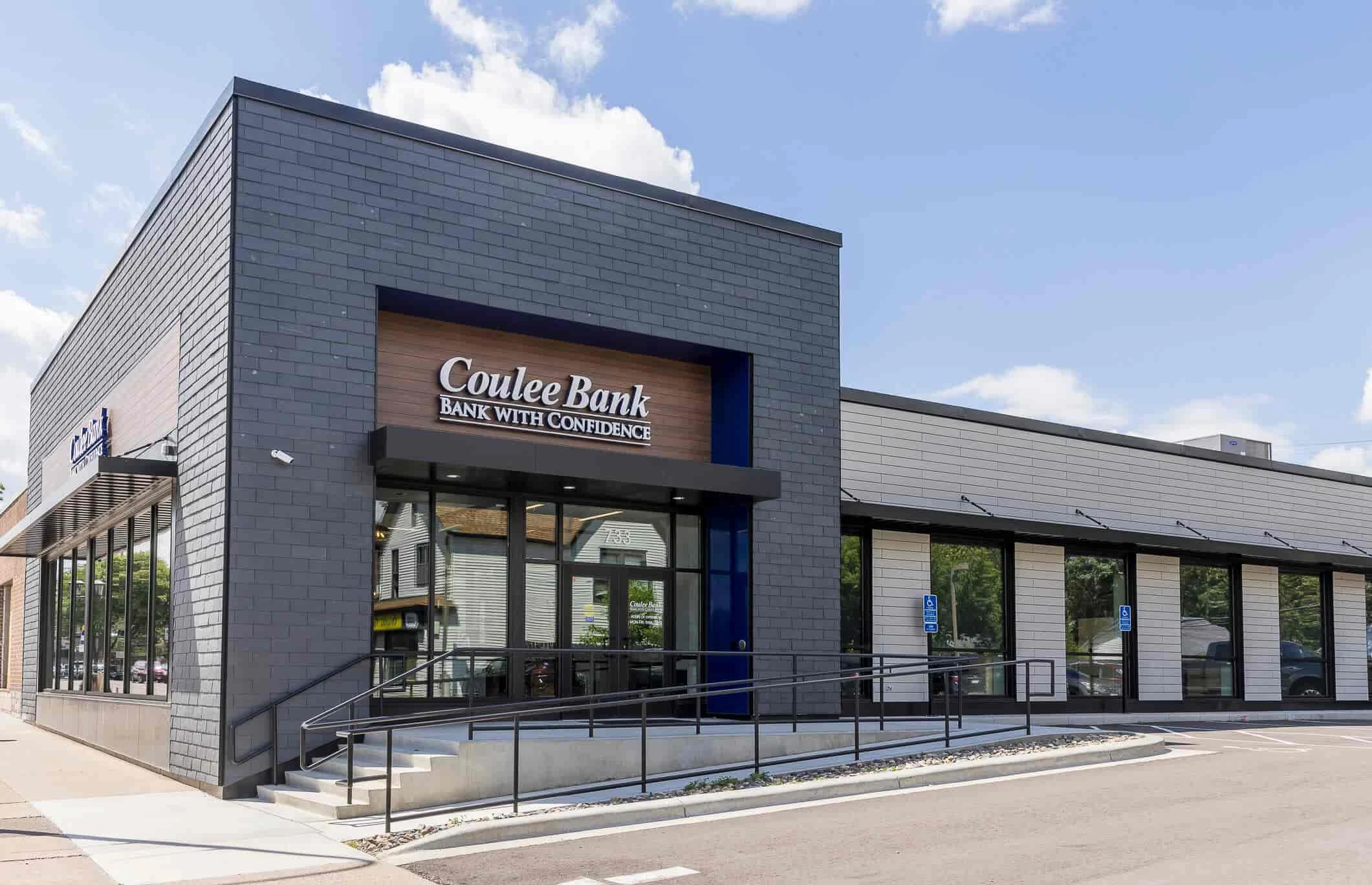 Modern bank building with grey brick exterior, large windows, and a prominent sign reading "Coulee Bank: Bank with Confidence." The scene is bright and inviting.