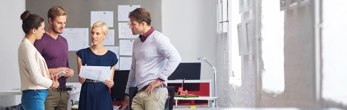 Group of four colleagues having a discussion in a modern office, reviewing documents together.