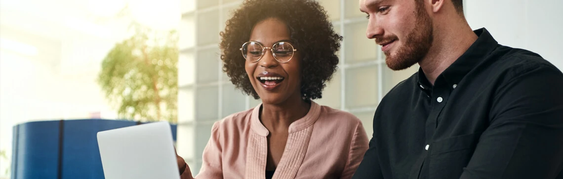 Two colleagues smiling and looking at a tablet together in a bright, modern office.