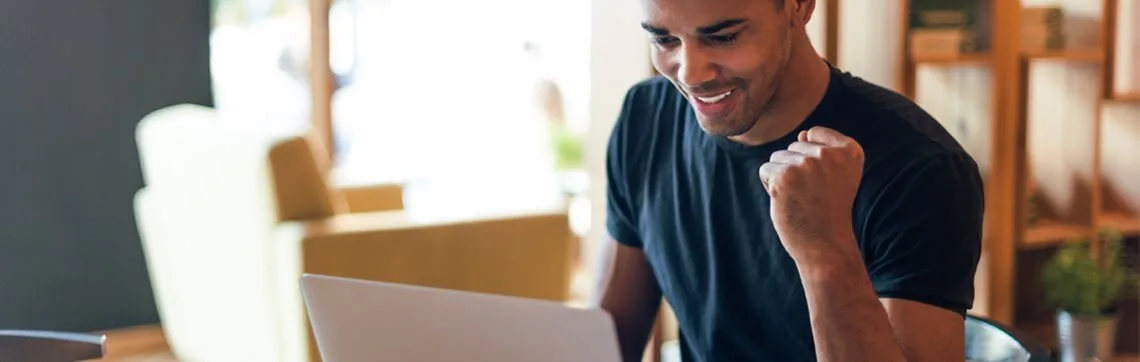 Young man looking at a computer and raising his fist in excitement.