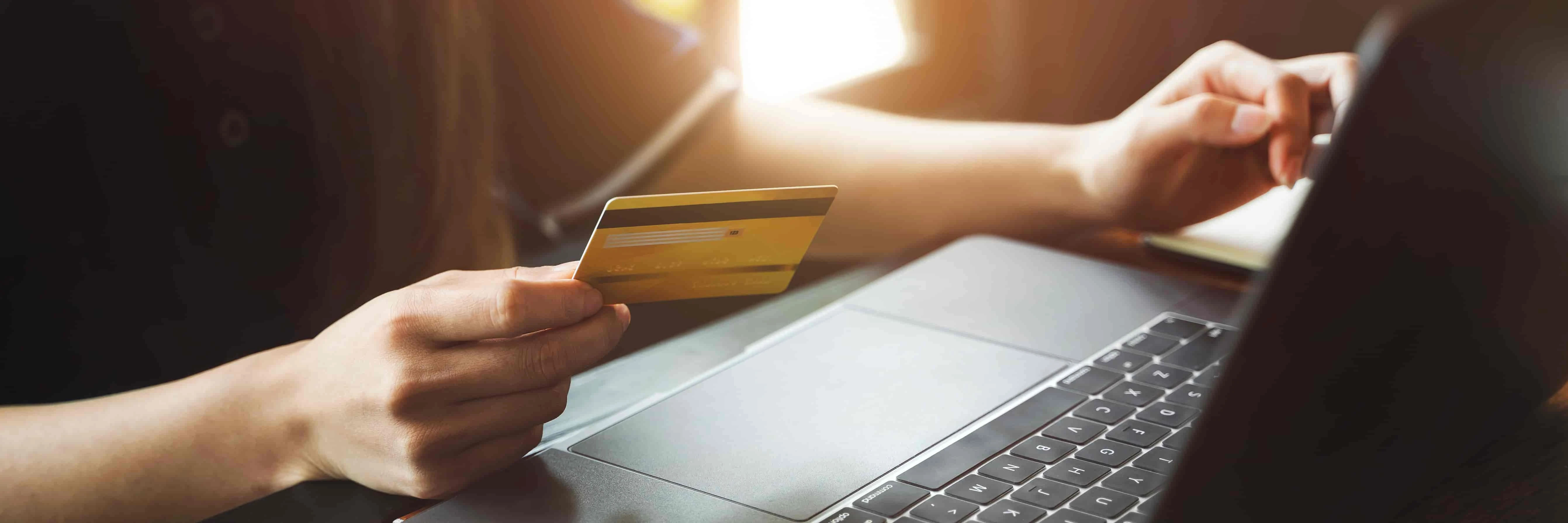 Person holding a credit card while using a laptop.