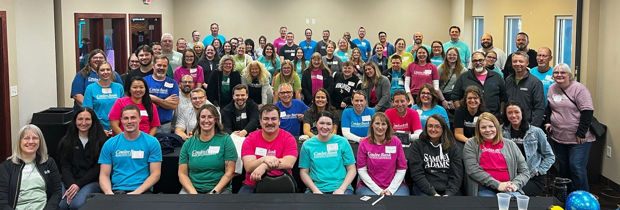 Large group of people with brightly colored shirts sitting and standing in a room.