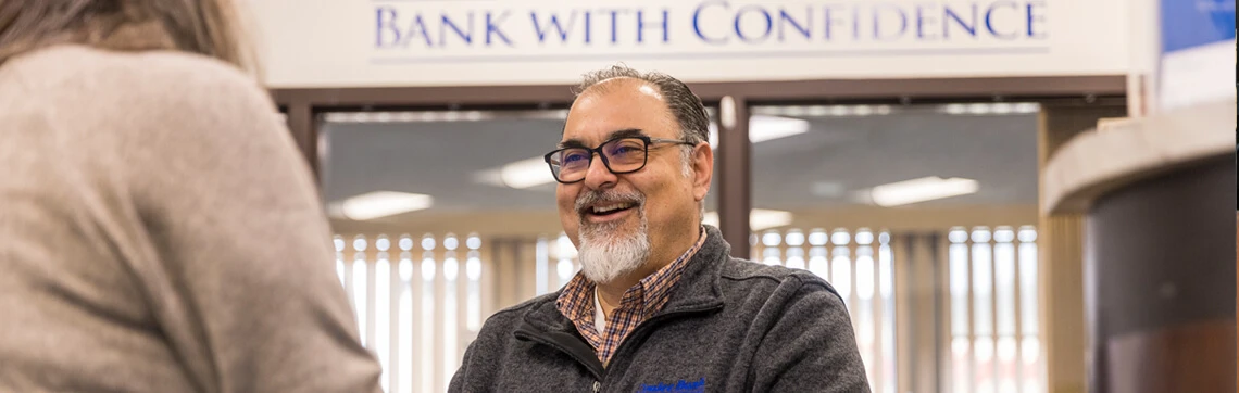 Man with classes smiling inside of a building helping another person.
