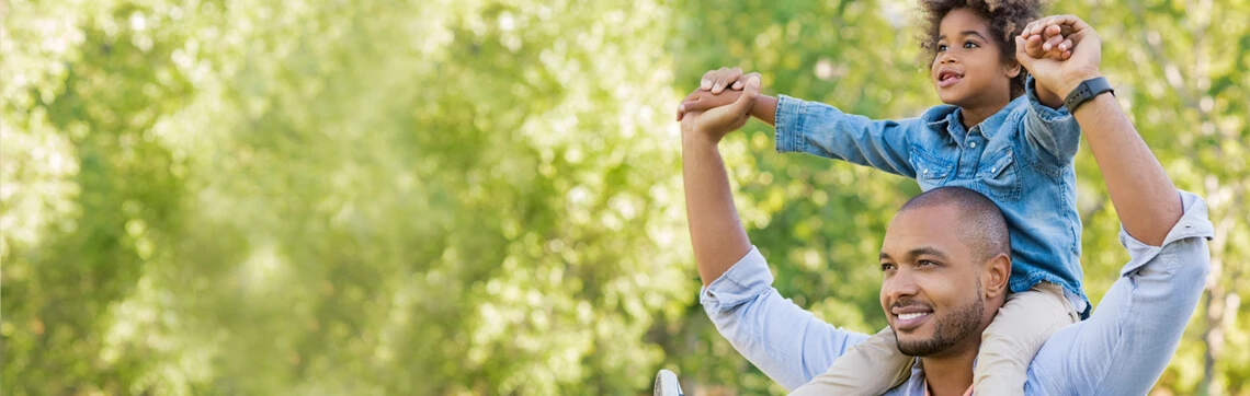 Smiling father carrying his child on his shoulders in a sunny park.