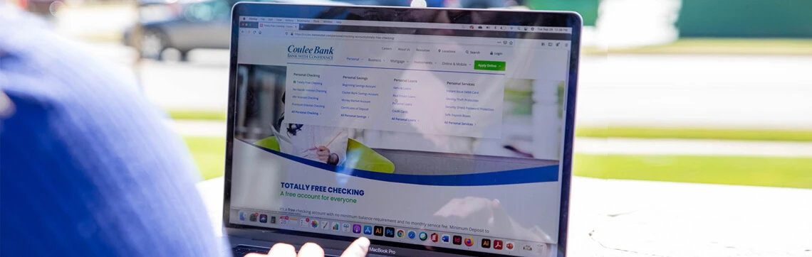 Person using a MacBook Pro to browse Coulee Bank’s website outdoors.
