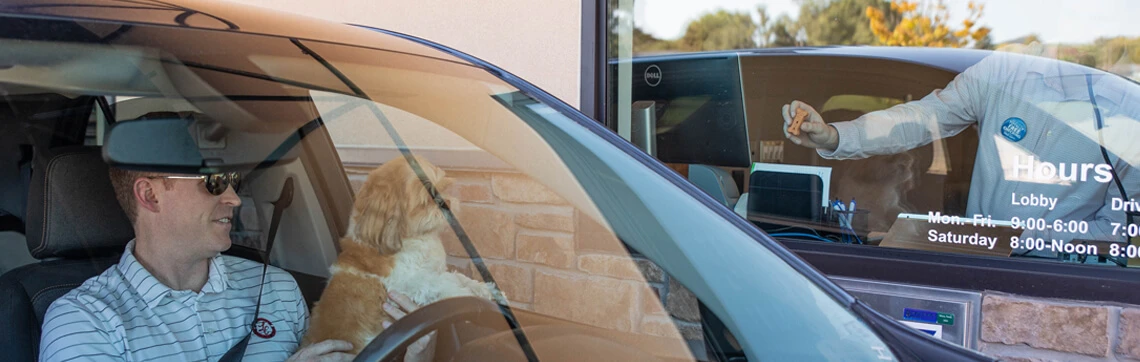 Man with a dog in his car at a bank drive-thru window.