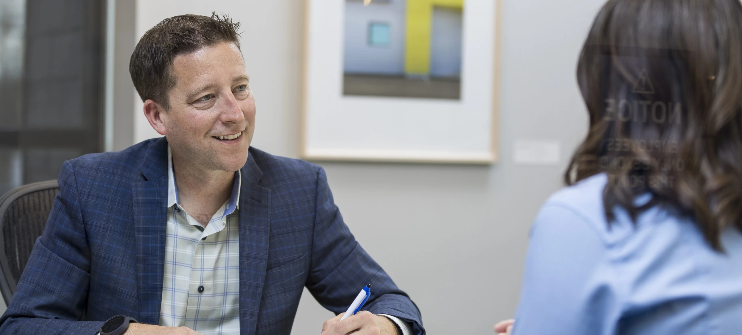 Business Banker helps a customer at his desk. He is holding a pen and writing on a document. 