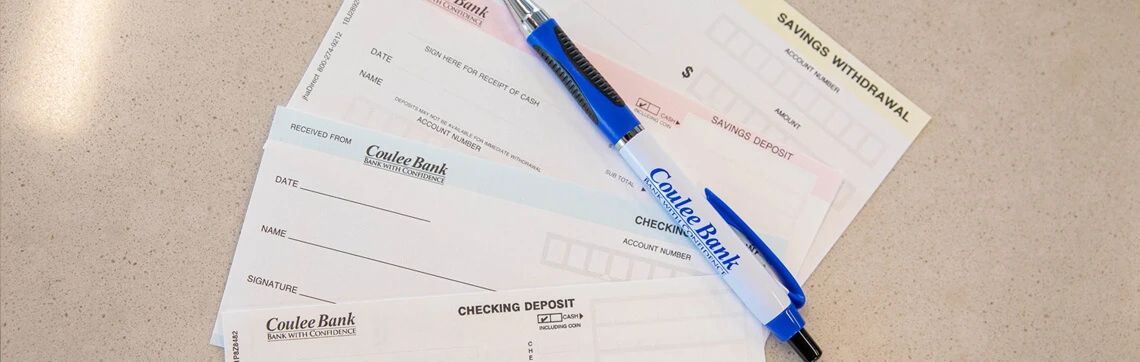 Coulee Bank deposit and withdrawal slips with a Coulee Bank pen on a countertop.