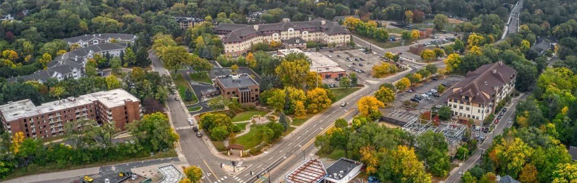 Aerial view of a residential area with autumn trees in vivid colors. Buildings and winding roads intersect around green spaces, conveying a serene, organized community setting.