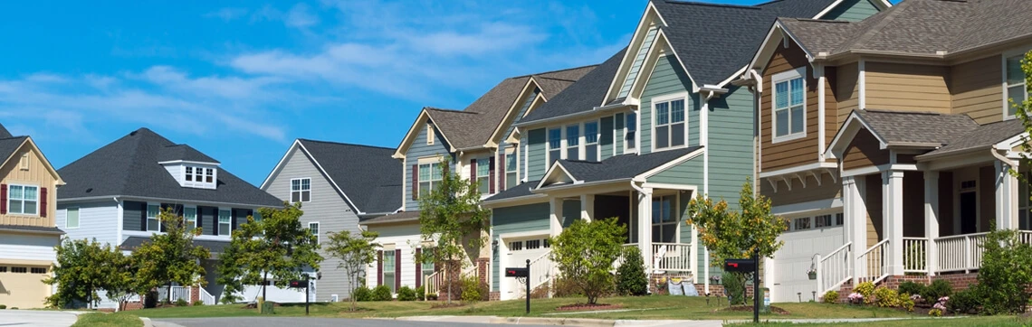 Row of suburban houses with driveways and front yards on a sunny day.
