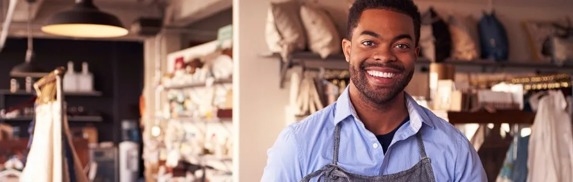 Smiling man wearing an apron standing in a home goods or craft store.