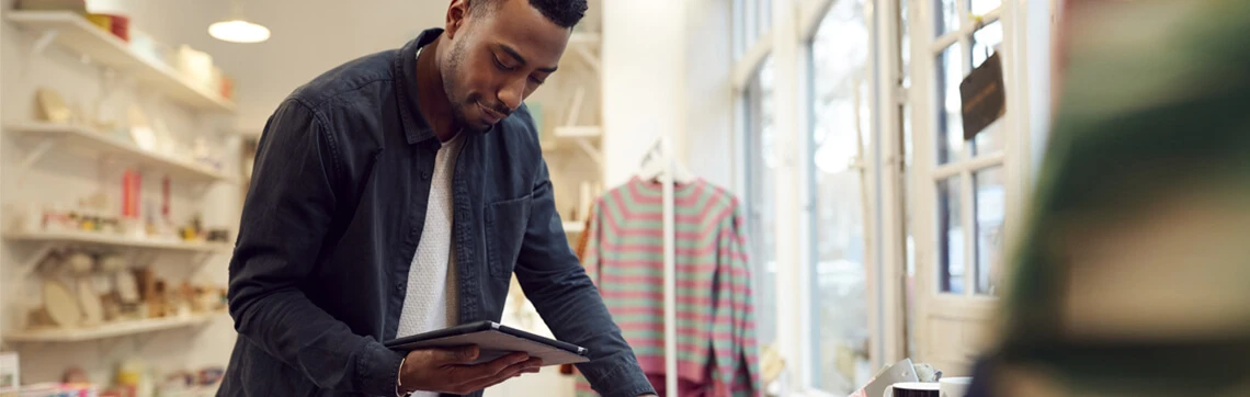 Man using a tablet while standing at a counter in a boutique-style retail store.