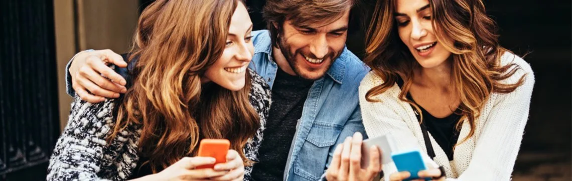 A group of three people sit closely, smiling and looking at their smartphones. They exude happiness and camaraderie, creating a warm, friendly atmosphere.