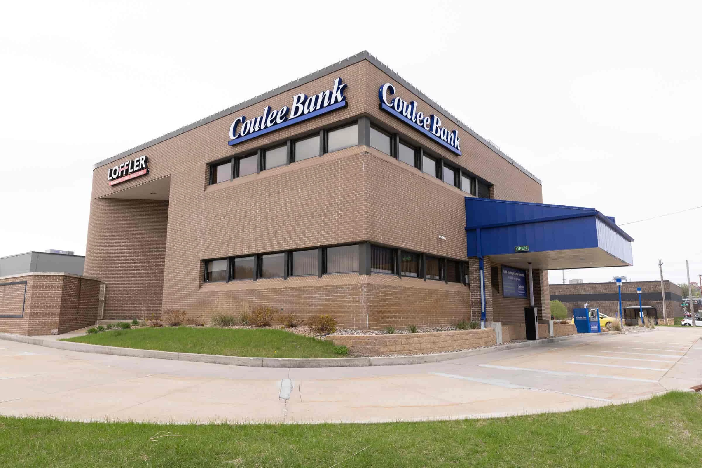 Brick building labeled "Coulee Bank" with drive-thru on the right. Overcast sky, neatly trimmed grass in front. Tone: professional, inviting.